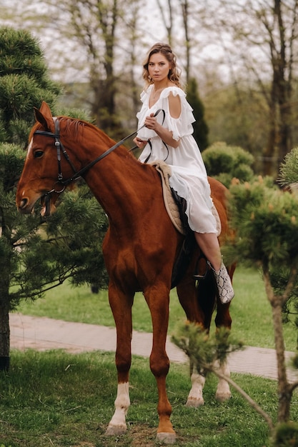 Une femme en robe d'été blanche à cheval près d'une ferme