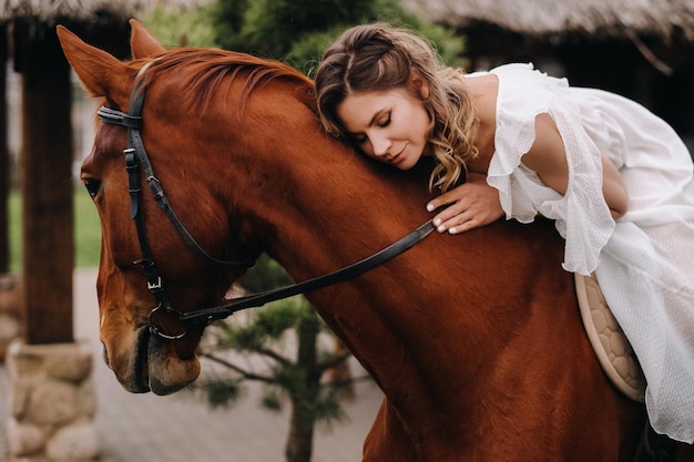 Une femme en robe d'été blanche à cheval près d'une ferme