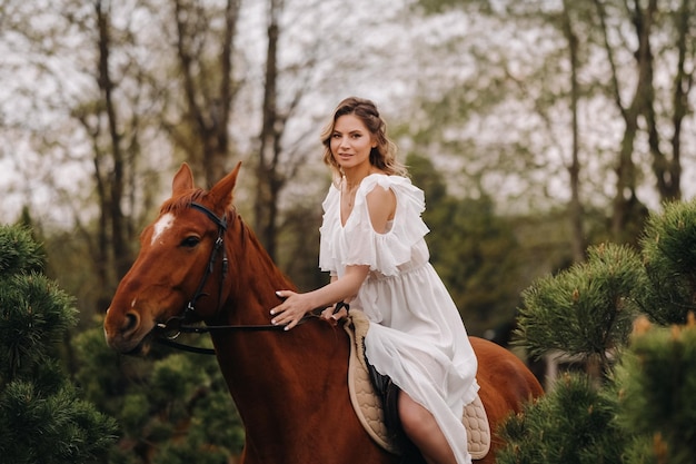 Une femme en robe d'été blanche à cheval près d'une ferme