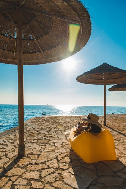 Femme en robe d'été jaune allongée sur un canapé jaune sur la plage de la mer