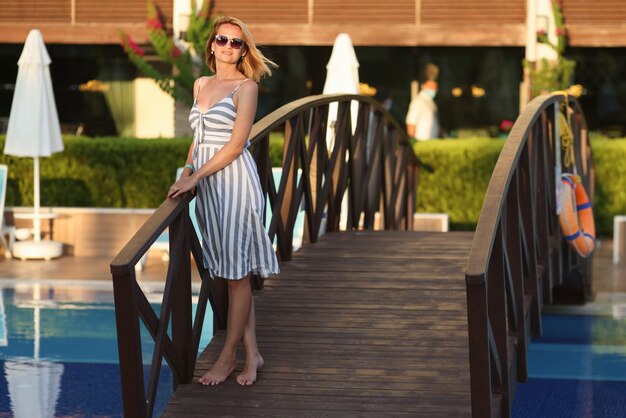 Femme en robe d'été se tient à côté d'un petit pont sur le terrain de l'hôtel