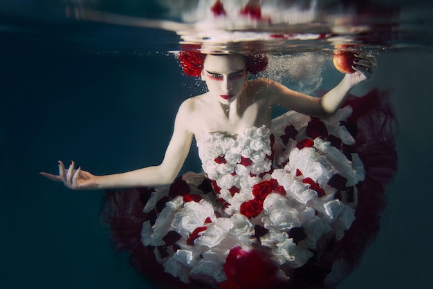 Femme en robe faite de roses blanches et rouges sous l'eau. Conte de fées, art, concept de mode