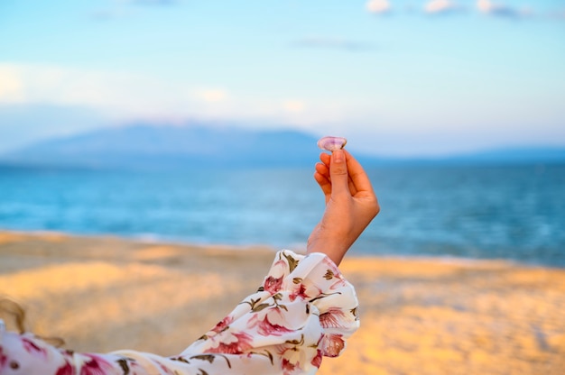 Femme en robe fleur rose tenant un coquillage sur la mer et les montagnes