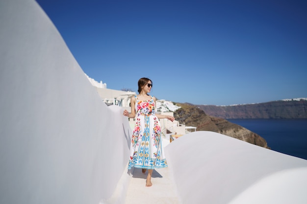 Femme en robe de flore sur le toit blanc d'un immeuble à Santorin, Grèce.