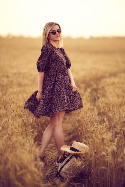 Femme en robe imprimée animale chapeau de paille dans un champ de blé