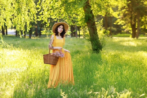 Femme en robe jaune et chapeau de paille avec un panier de pique-nique en été