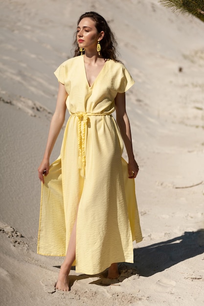 Une femme en robe jaune se tient dans le sable.