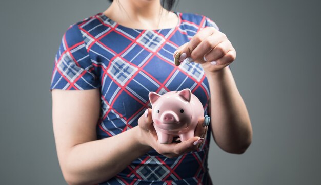 Une femme en robe jette une pièce de monnaie dans une tirelire