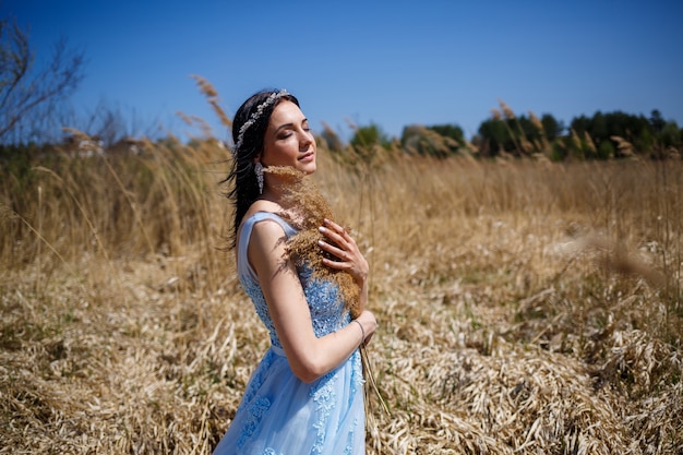 Femme en robe longue bleue dans les roseaux. Portrait de mode avec des fleurs séchées