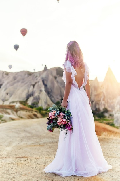 Femme en robe longue sur fond de ballons en Cappadoce. Fille aux mains de fleurs se dresse sur une colline et regarde un grand nombre de ballons volants. Turquie Cappadoce paysage de conte de fées de montagnes