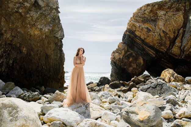 Femme en robe longue près des rochers et de l'océan