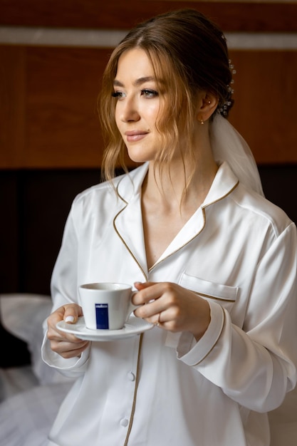 Une femme en robe de mariée tient une tasse de café à la main.