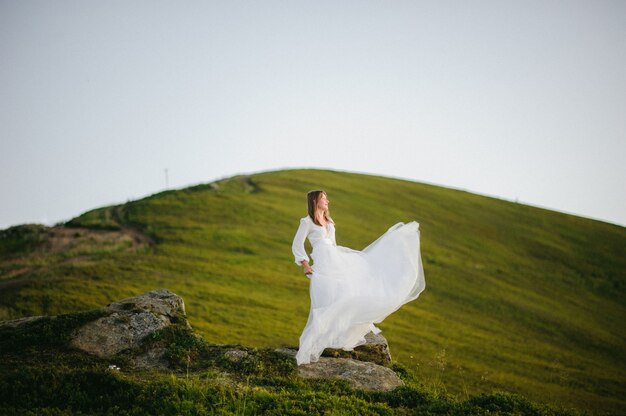 Femme en robe de mariée traverse le champ vers les montagnes