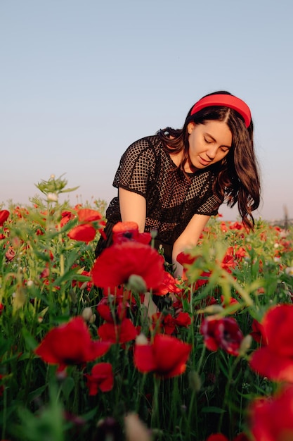 Femme en robe noire au coucher du soleil sur le champ de fleurs de coquelicots