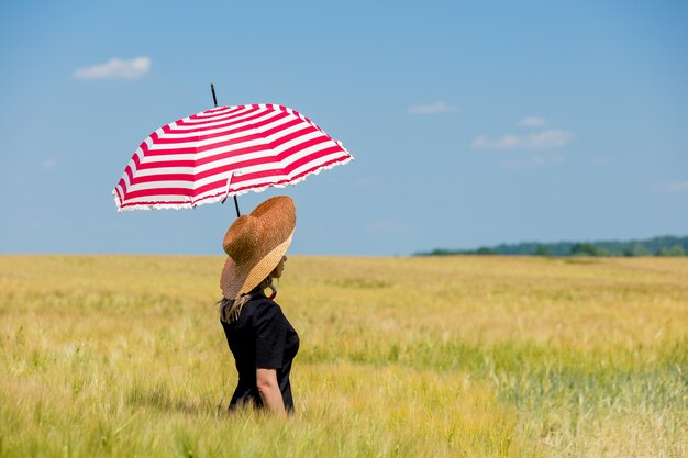 Femme en robe noire et chapeau avec parapluie rouge rester dans le champ de blé