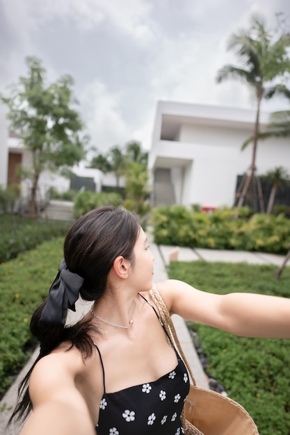 Femme en robe noire avec panier de paille marchant dans un hôtel de villégiature tropical