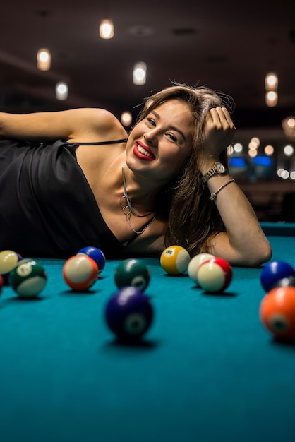 Femme en robe noire près des boules allongées sur une table de billard Détendez-vous avec un style de vie de jeu de billard