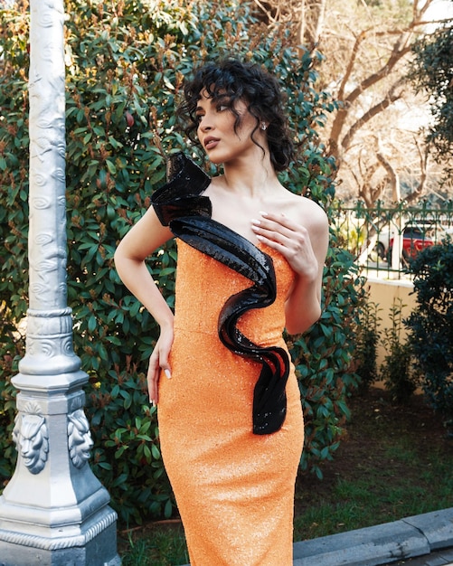 Une femme en robe orange pose devant un arbre.