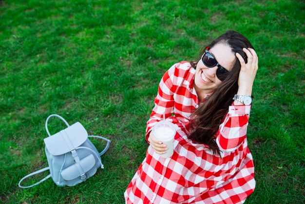 Femme en robe rouge buvant un smoothie assis sur du gras vert