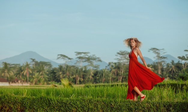 Une femme en robe rouge et chapeau se promène dans les rizières à Bali