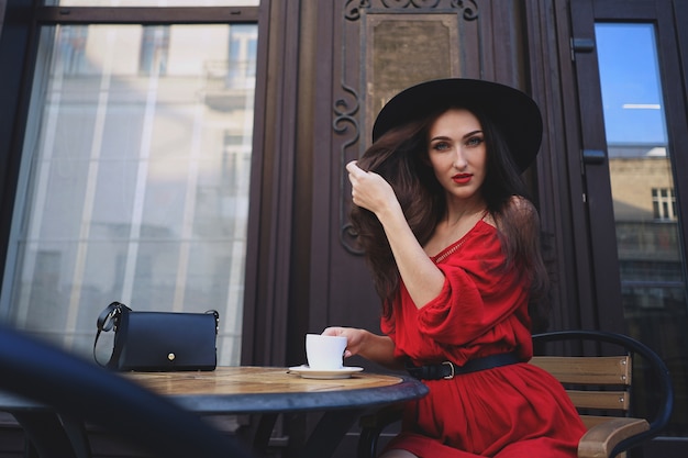 Femme en robe rouge et chapeau vintage avec une tasse de café