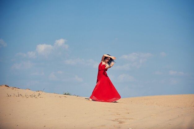 Femme en robe rouge dansant dans le désert au ciel bleu