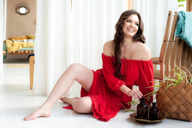 Une femme en robe rouge est assise par terre à côté d'une plante