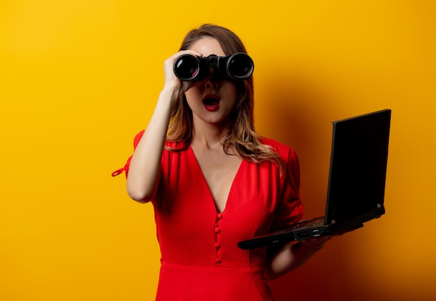 femme en robe rouge avec jumelles et ordinateur portable