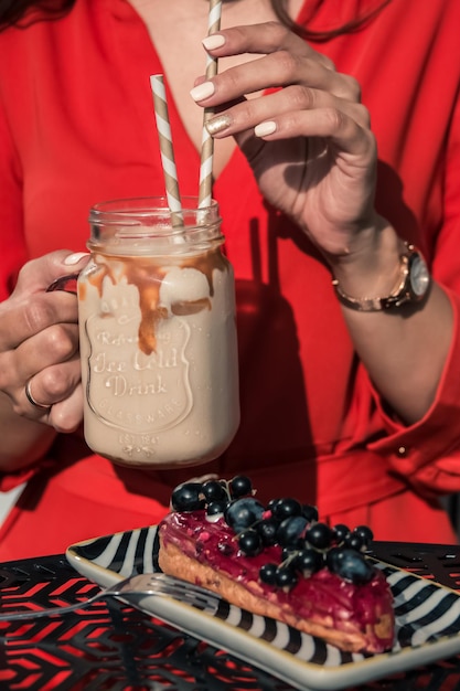 Une femme en robe rouge profite d'une boisson glacée rafraîchissante et d'un éclair de dessert français traditionnel dans un café