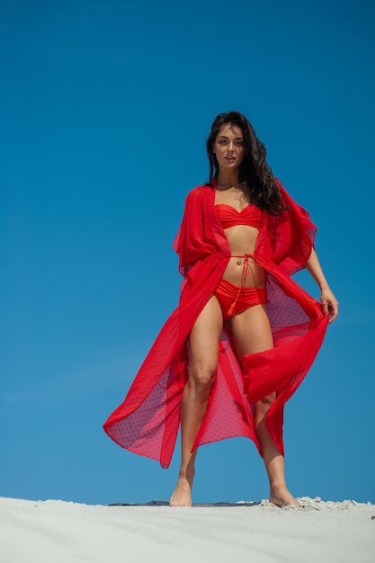 Une femme en robe rouge se dresse sur un mur devant un ciel bleu.