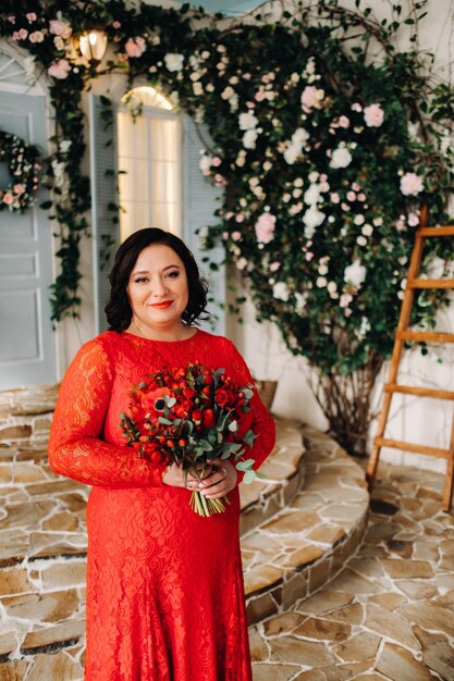 Une femme en robe rouge se dresse et tient un bouquet de roses rouges et de fraises à l'intérieur.