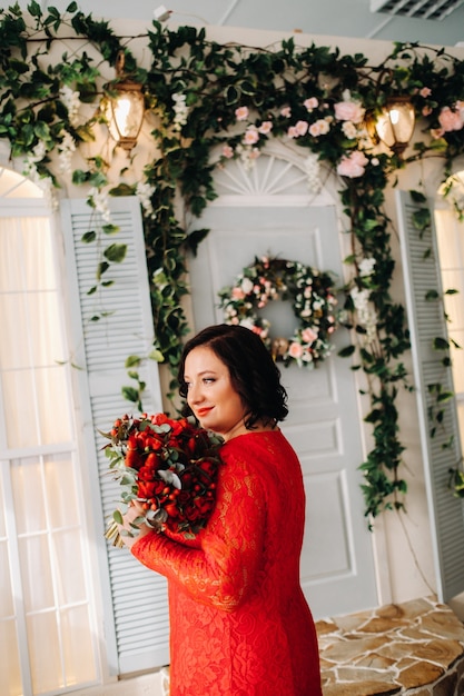 Une femme en robe rouge se dresse et tient un bouquet de roses rouges et de fraises à l'intérieur.