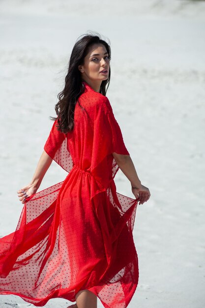 Une femme en robe rouge se promène sur la plage