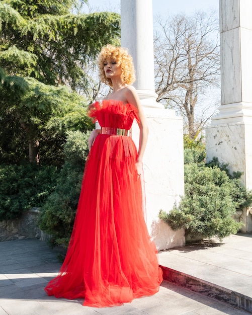 Une femme en robe rouge se tient sur un trottoir devant une colonne blanche.