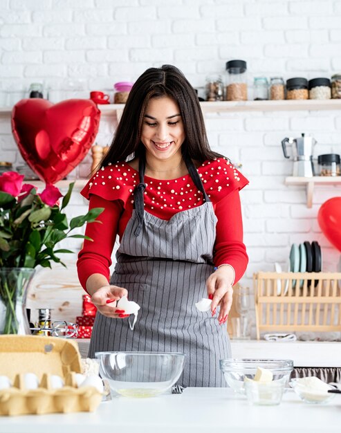 Femme en robe rouge et tablier gris faisant des cookies de la Saint-Valentin dans la cuisine