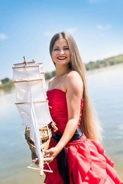 Femme en robe rouge tenant le modèle de bateau sur la plage