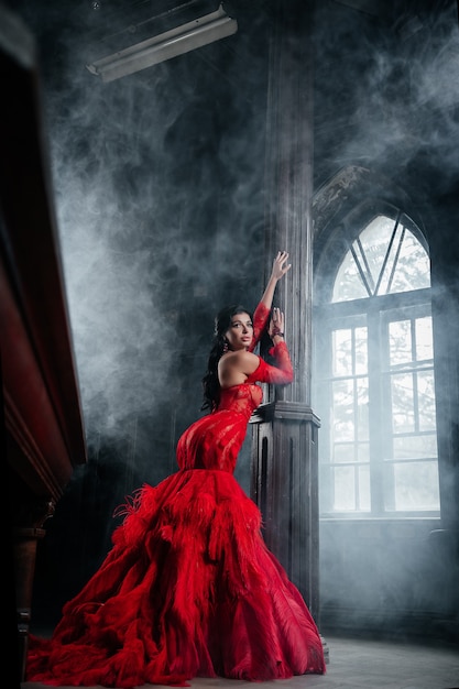 Femme robe rouge vintage vieux château belle princesse en robe séduisante histoire de conte de fées femme caucasienne élégante près de grande fenêtre avec brouillard de fumée