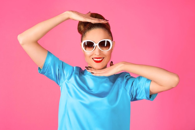 femme en robe de soie bleue et lunettes de soleil blanches sur fond rose