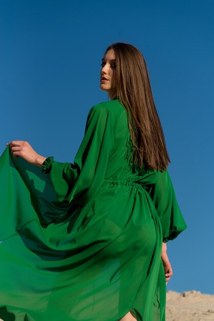 Une femme en robe verte se tient devant un ciel bleu.