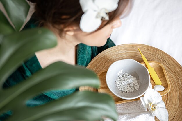 Photo femme en robe verte tenant une assiette avec masque d'argile et fleur d'orchidée, vue de dessus, concept de soins spa.