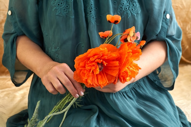 Femme en robe verte tenant des fleurs de pavot, gros plan sur ses mains. Rêves de printemps.