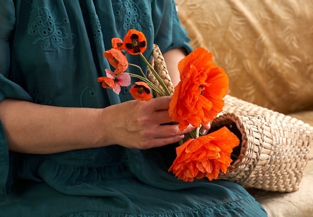 Femme en robe verte tenant des fleurs de pavot, gros plan sur ses mains. Rêves de printemps.