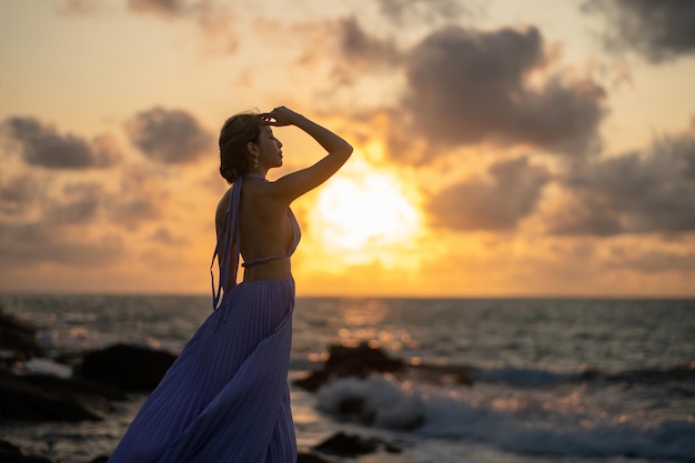 Femme en robe violette sur la plage, profitez d'un moment romantique au coucher du soleil.