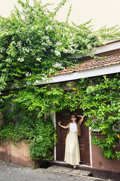 Femme romantique debout près de vieilles portes sous un buisson de bougainvilliers en fleurs