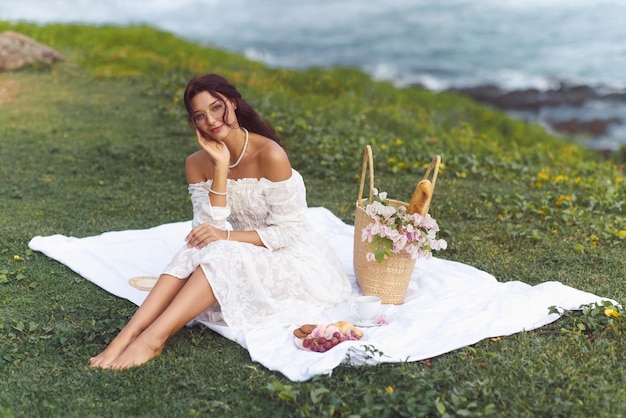 Femme romantique élégante pique-niquer dans un pré d'été près de la mer