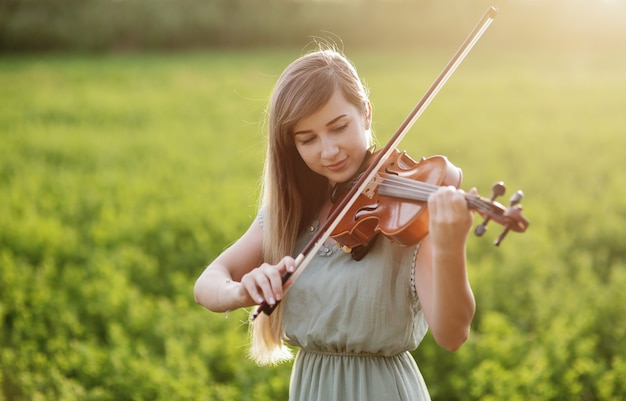 Femme romantique, fille aux cheveux lâches jouant du violon. Lumière du coucher du soleil dans la nature