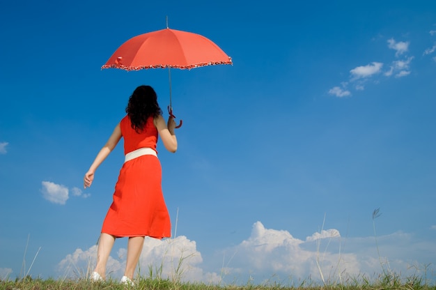 Femme en rouge avec parapluie et ciel bleu