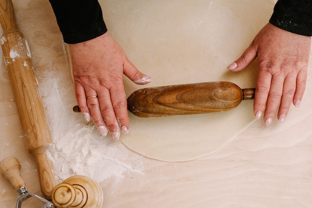 Une femme roule la pâte pour des boulettes et des plats cuisinés, avec un rouleau à pâtisserie en bois foncé. Le cuisinier fait la pâte. Vue de dessus
