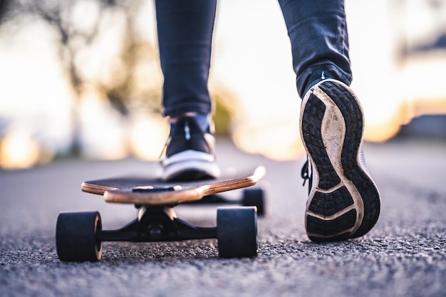 Une femme roule sur une route droite sur un longboard au coucher du soleil Patineuse en tenue décontractée s'entraînant à bord pendant le coucher du soleil avec une lumière orange Une fille tient un longboard dans les mains