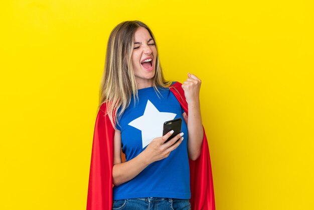 Femme roumaine de super héros isolée sur fond jaune avec téléphone en position de victoire